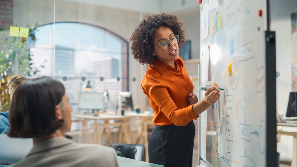 Young Black professional leading a team meeting at a whiteboard