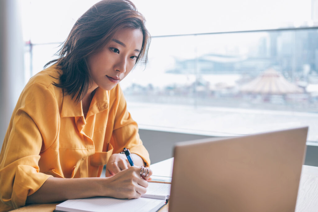 Young professional looking at a laptop and taking notes