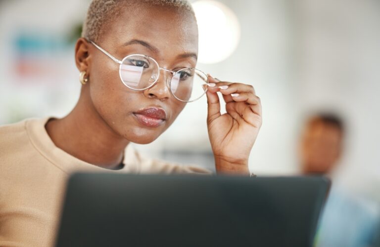 Young Black professional looking closely at her laptop and holding her glasses