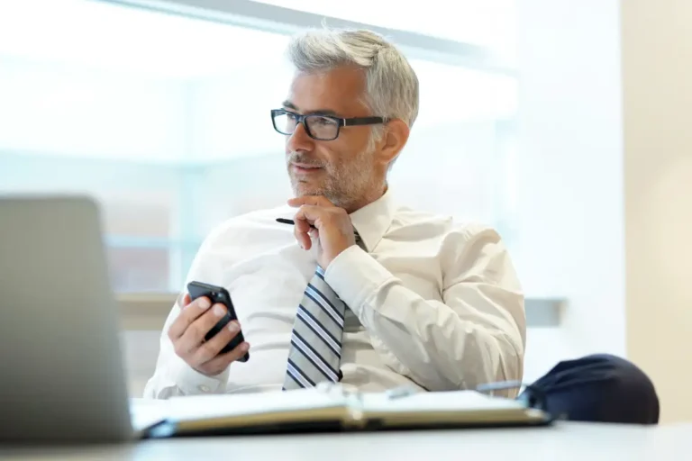 Older professional man holding phone and thinking