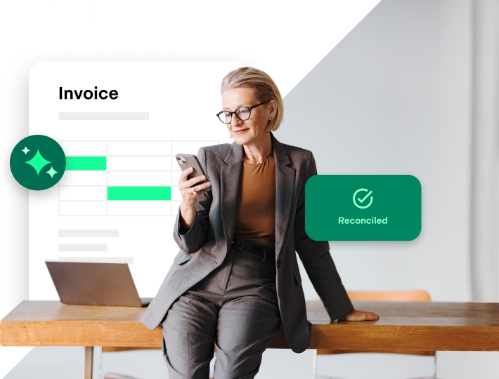 Professional woman wearing glasses looking at her phone. Background shows invoice sheet and the word reconciled with green check