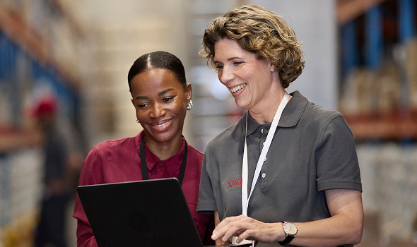 Two people stand, smiling while working on a laptop together