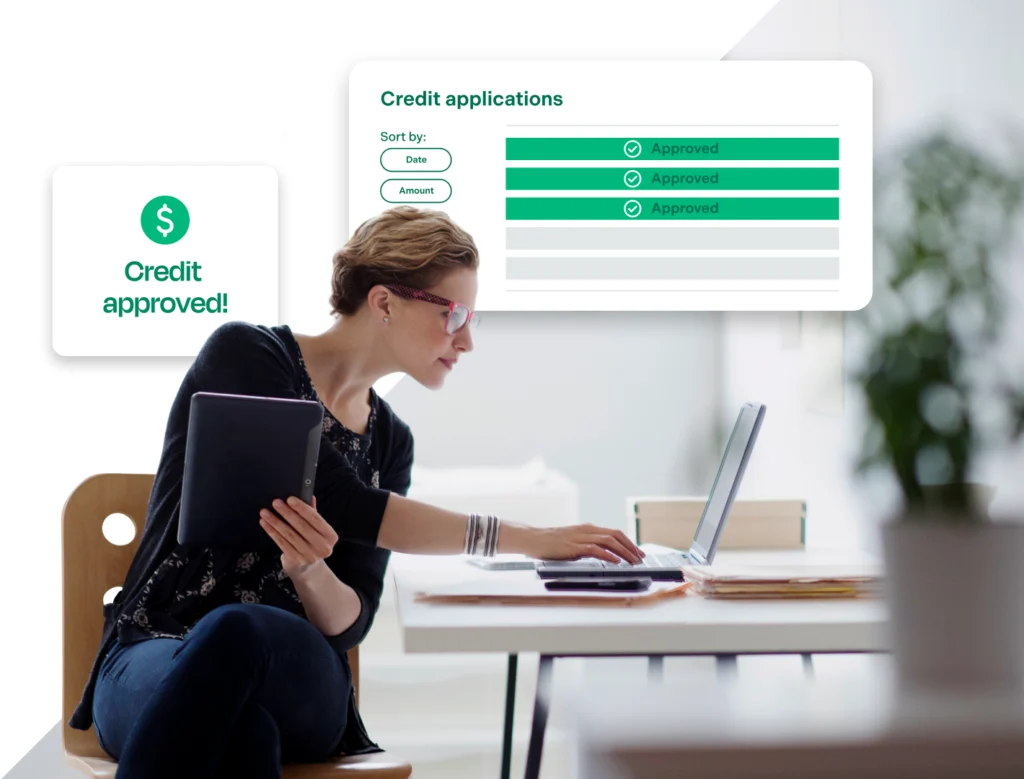 A person works simultaneously on a tablet and a laptop, with graphics related to credit applications overlaid