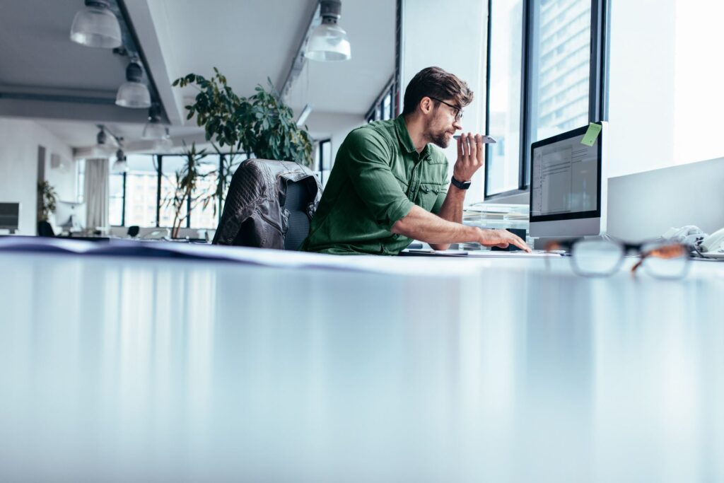 Man working at his desk on a computer while speaking into his mobile phone