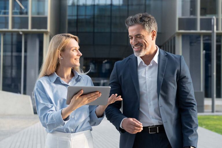Man and woman walking outside while discussing what they are viewing on a tablet