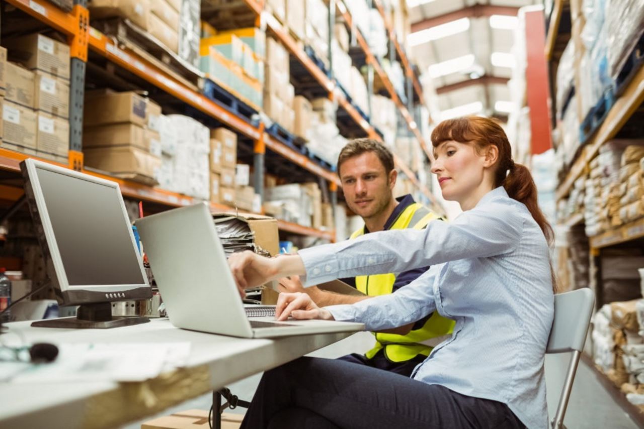an image of a woman and a man in a warehouse at a table looking at a laptop together
