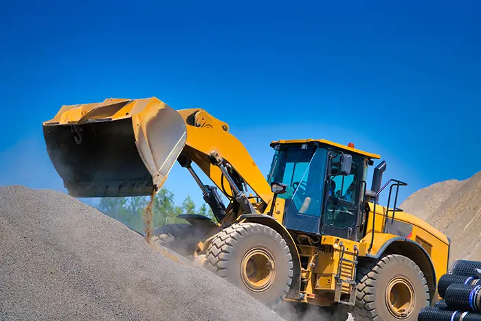 Heavy equipment loader driving up pile of gravel