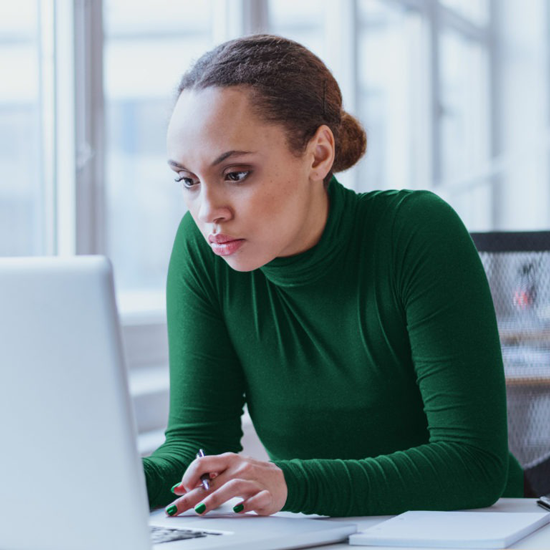 Woman holding a pen seated in front of office windows