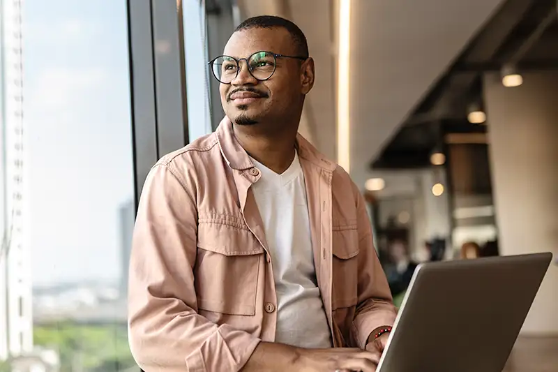 young developer holding laptop and looking out window