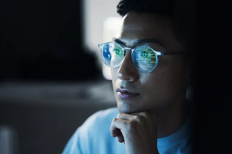 young man looking at computer in dark room with code reflected in glasses