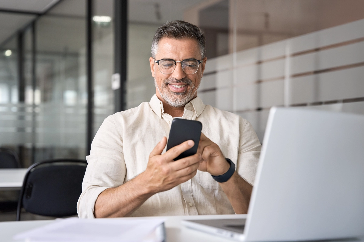 Man looking at phone reading Billtrust blog: Suppliers can’t avoid payment processing costs, but they can control them