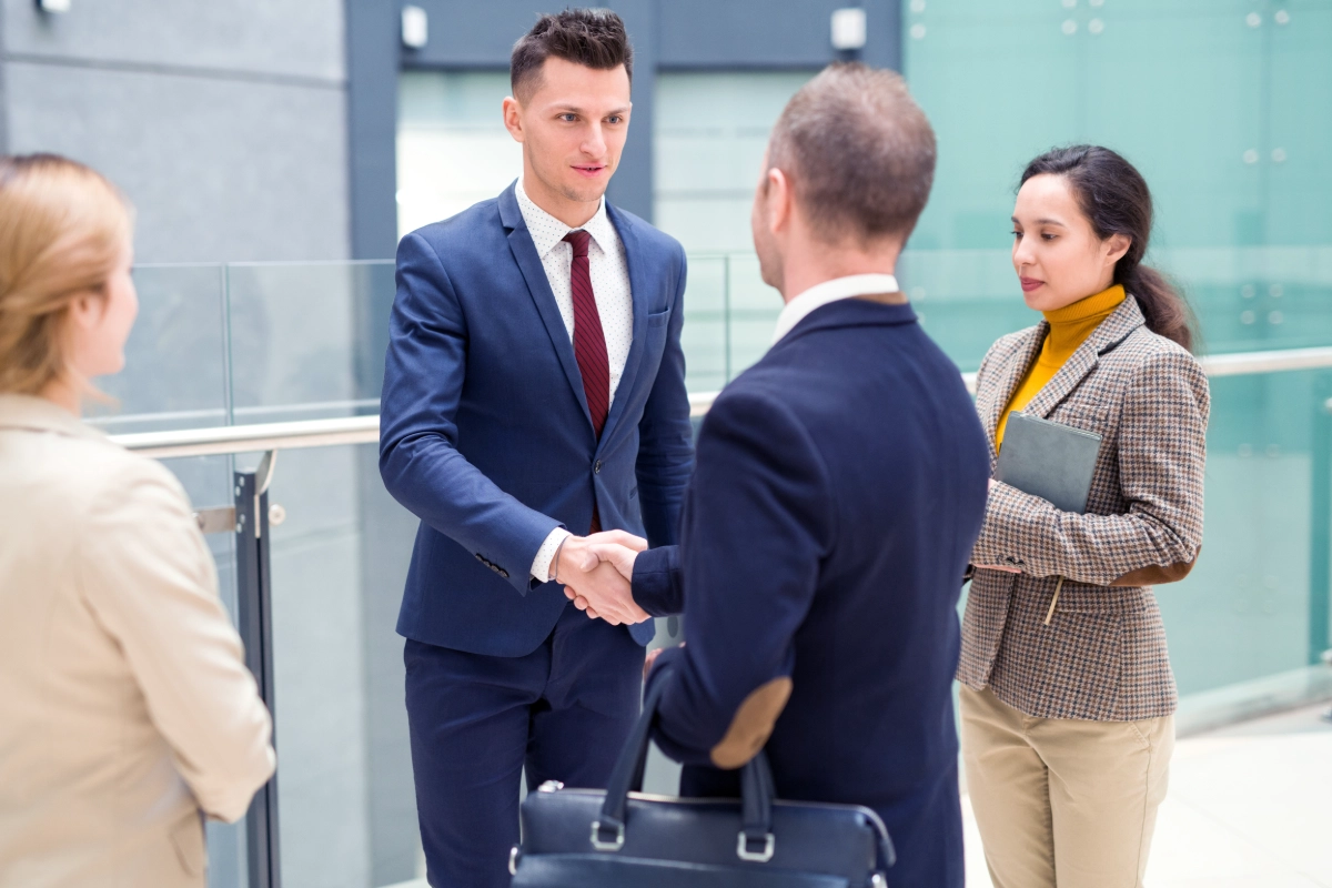 Man shacking hand with another man in an office room full of people