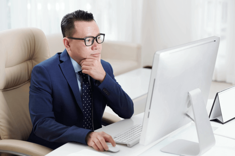 Man wearing glasses sitting at desk looking at desktop monitor
