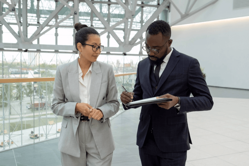 Man in suite writing on note pad while talking to woman in office building