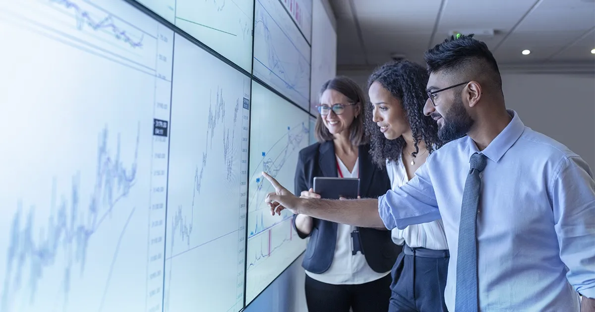 Man pointing at graph on screen standing next to two women