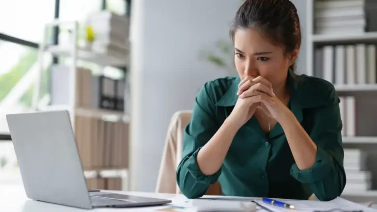 women wearing green shirt in office looking at computer deep in thought