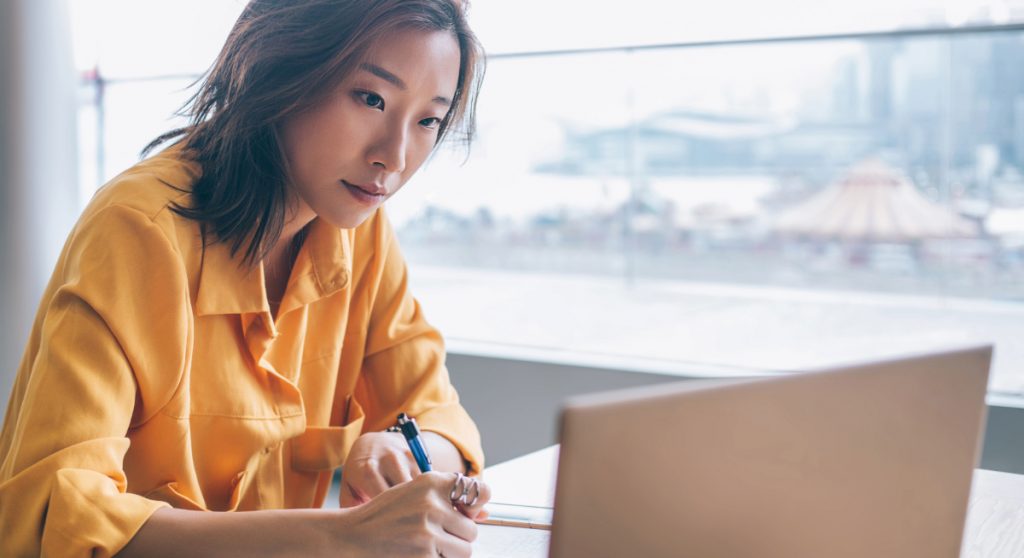 Young professional looking at a laptop and taking notes