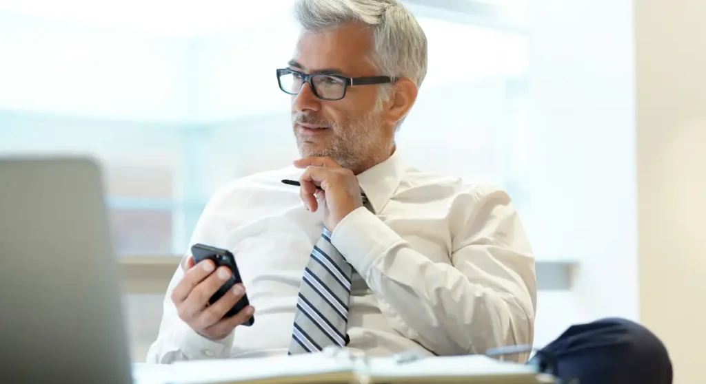 Older professional man holding phone and thinking
