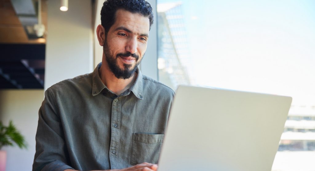 Smiling young businessman working on a laptop by an office window