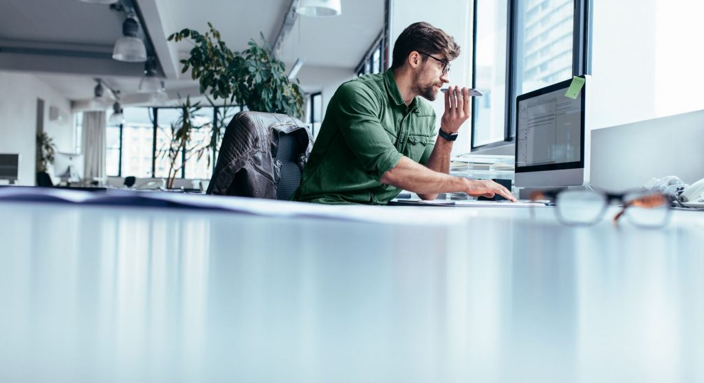 Man working at his desk on a computer while speaking into his mobile phone