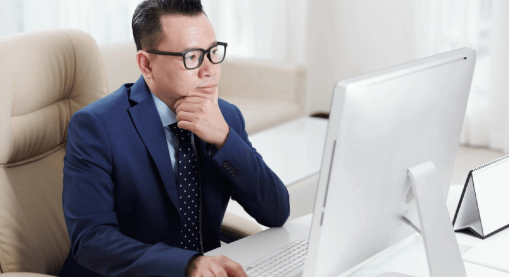 Man wearing glasses sitting at desk looking at desktop monitor