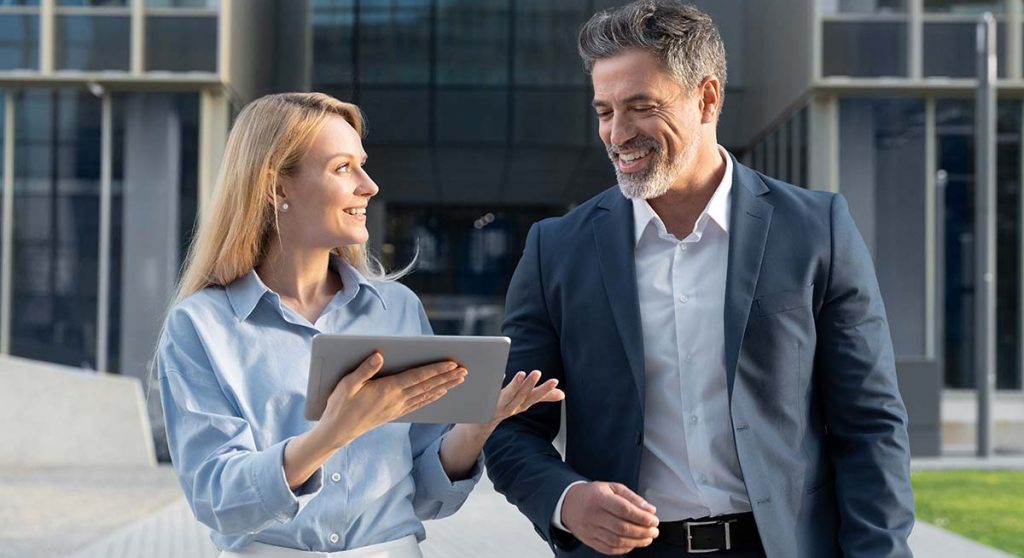 Man and woman walking outside while discussing what they are viewing on a tablet