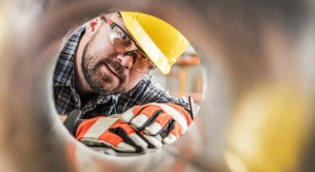 Mann mit Schutzhelm, der ein Manometer justiert