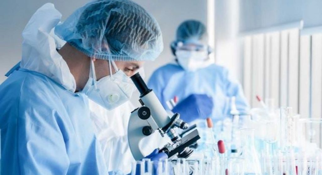 Scientists in protective gear look at microscopes