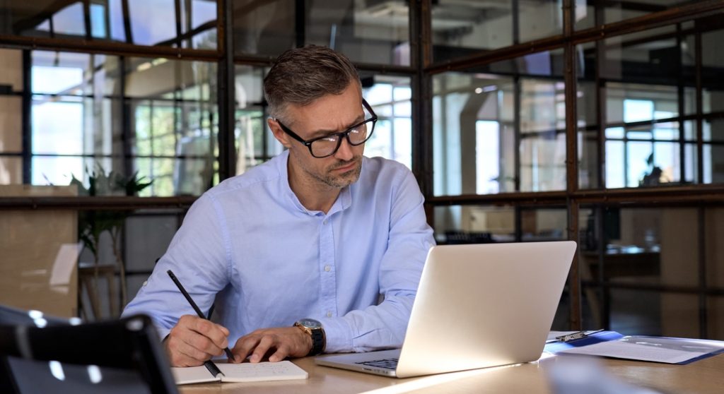 Professional looking at laptop and taking notes