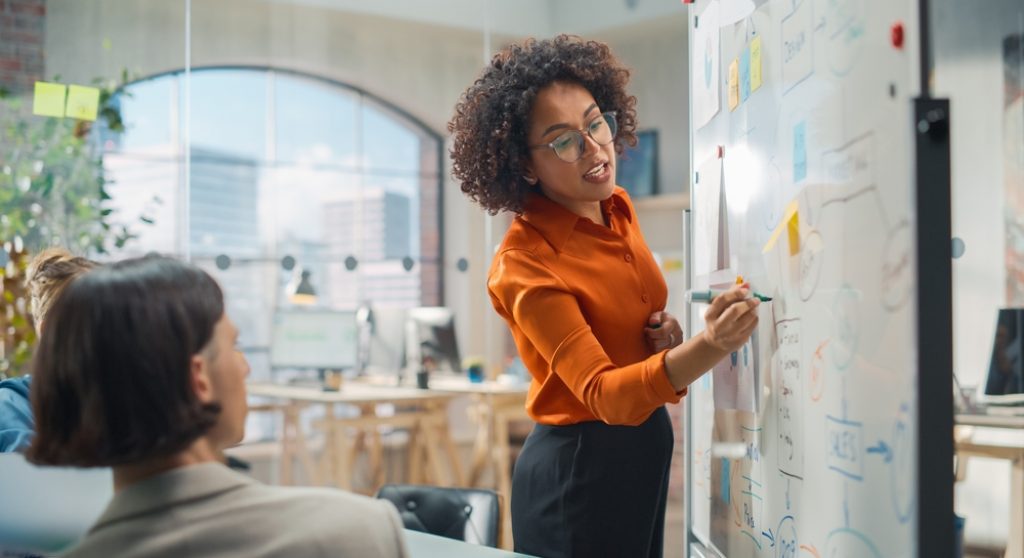Young Black professional leading a team meeting at a whiteboard