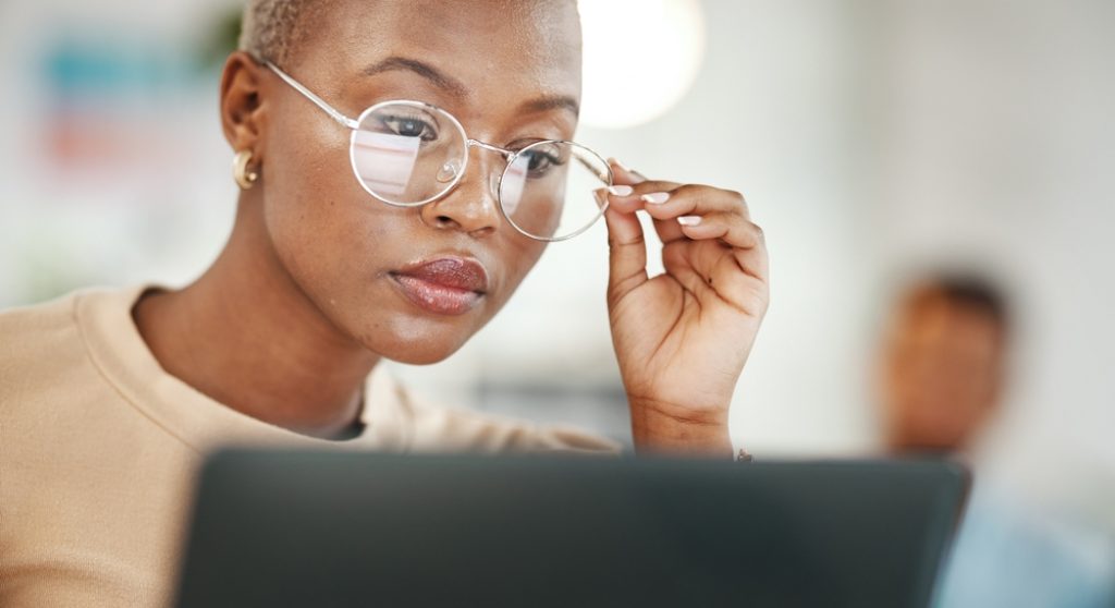 Young Black professional looking closely at her laptop and holding her glasses