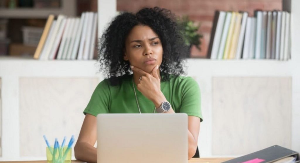 A woman sitting at a desk with laptop pondering
