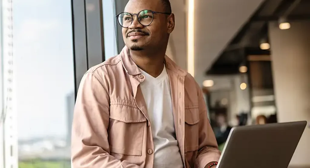 young developer holding laptop and looking out window